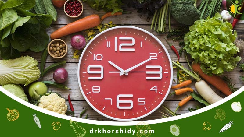 یک ساعت قرمز رنگ که وسط انوان میوه و سبزیجات مختلف وجود دارد